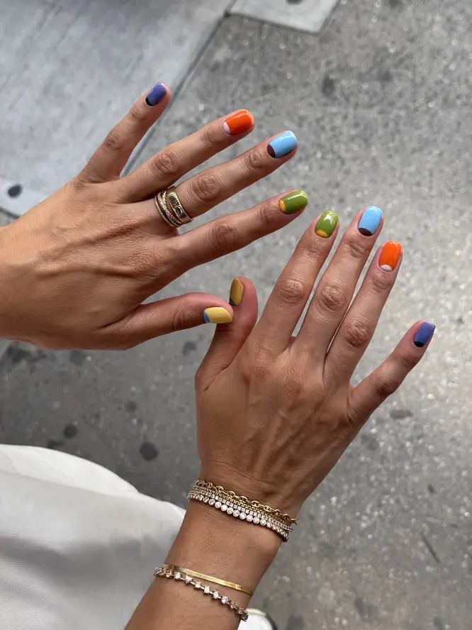 Colorblock nail art — orange, sky blue, olive and violet on short nails, New York street shot.