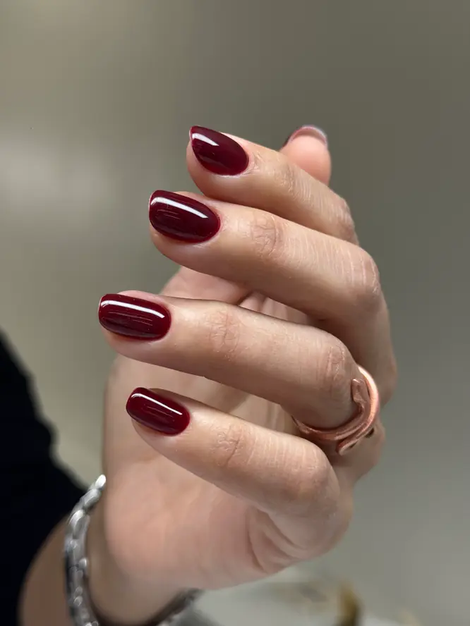 Deep-red gel gloss on round nails with a rose-gold ring — client manicure.