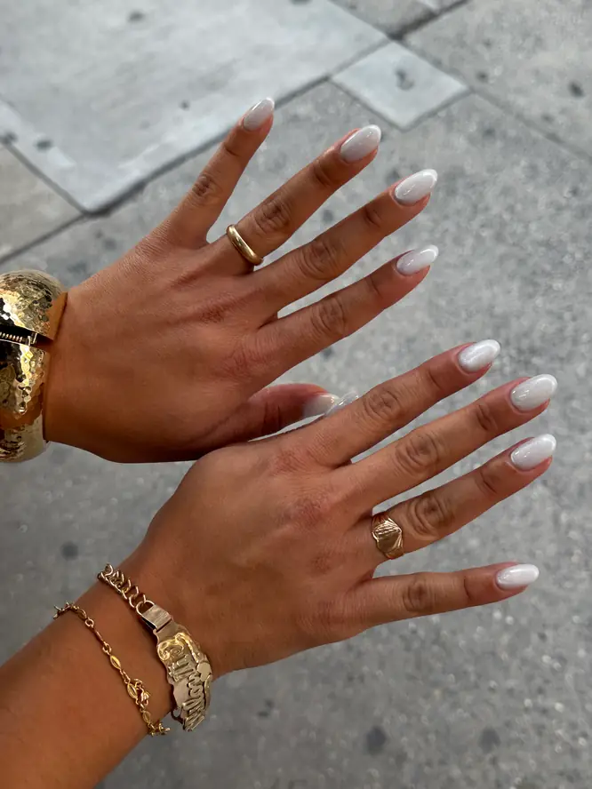 Pearl-white gel on almond nails with layered gold jewelry — client work, New York street shot.