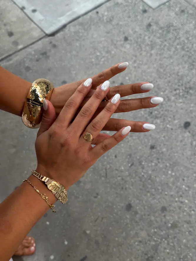 Pearl-white gel on almond nails with gold bangles, hands crossed — New York street shot.