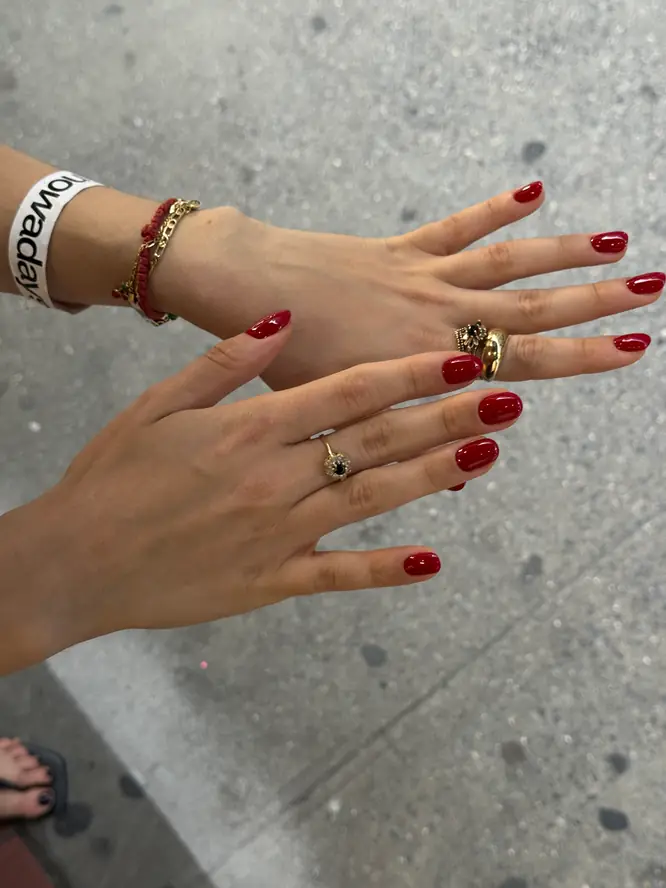Glossy red gel manicure on both hands with gold rings — client work, New York street shot.